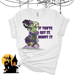 May include: White t-shirt with a green and purple illustration of a female zombie wearing a purple lingerie set. The text "If you've got it, haunt it" is printed in purple on the shirt.