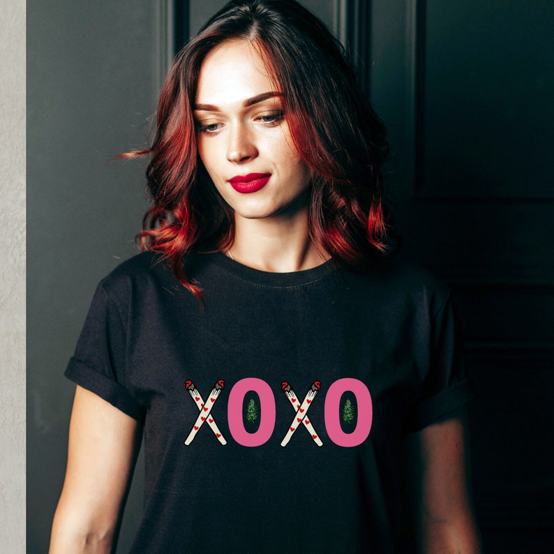 May include: A black t-shirt with a pink "XOXO" graphic featuring stylized candy canes and Christmas trees.