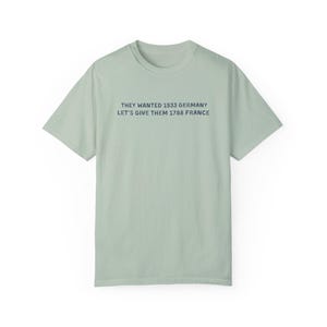 May include: A light green t-shirt with the text "THEY WANTED 1933 GERMANY LET'S GIVE THEM 1788 FRANCE" printed in dark blue. The shirt has short sleeves and a crew neck.
