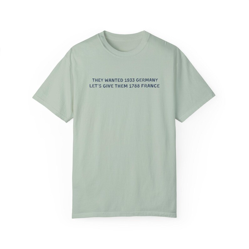 May include: A light green t-shirt with the text "THEY WANTED 1933 GERMANY LET'S GIVE THEM 1788 FRANCE" printed in dark blue. The shirt has short sleeves and a crew neck.