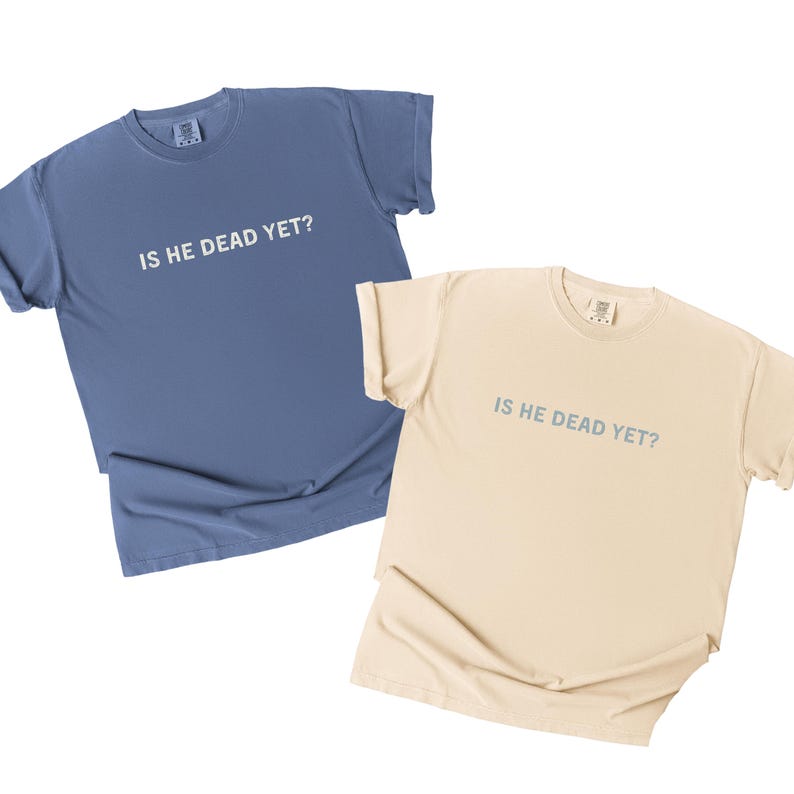 K&ouml;nnte beinhalten: Zwei T-Shirts mit dem Aufdruck "Is he dead yet?"  Ein T-Shirt ist hellblau und das andere beige.