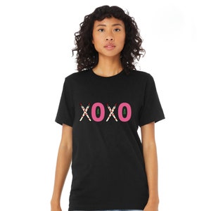 May include: Black t-shirt with a pink "XOXO" graphic made of candy canes. The candy canes have red and white stripes and green leaves.