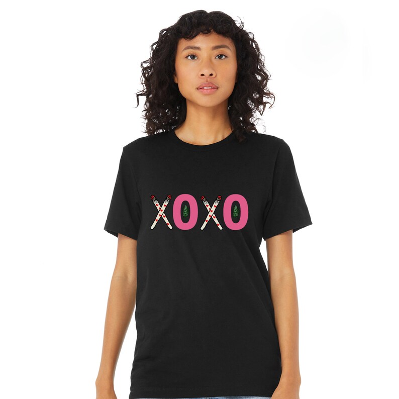 May include: Black t-shirt with a pink "XOXO" graphic made of candy canes. The candy canes have red and white stripes and green leaves.