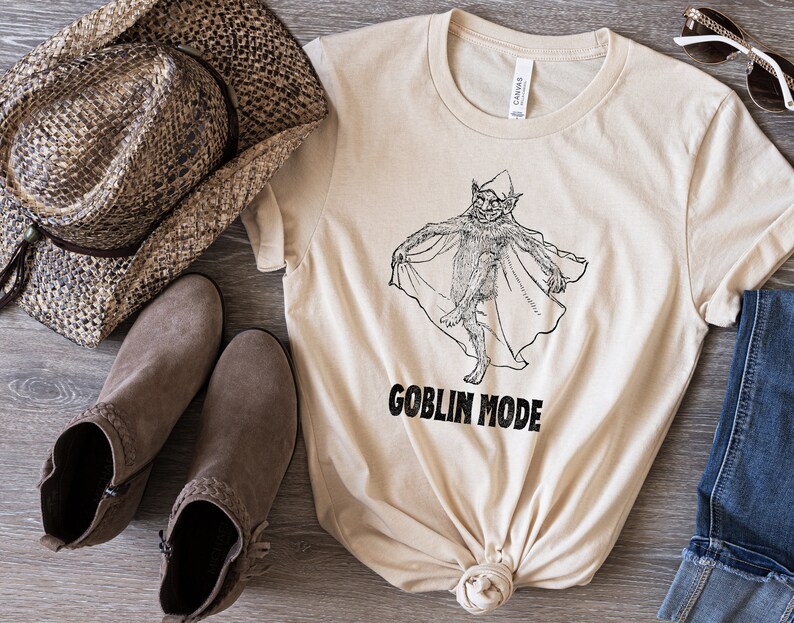 May include: A beige t-shirt featuring a black and white illustration of a goblin wearing a cape. The text "GOBLIN MODE" is printed beneath the illustration.