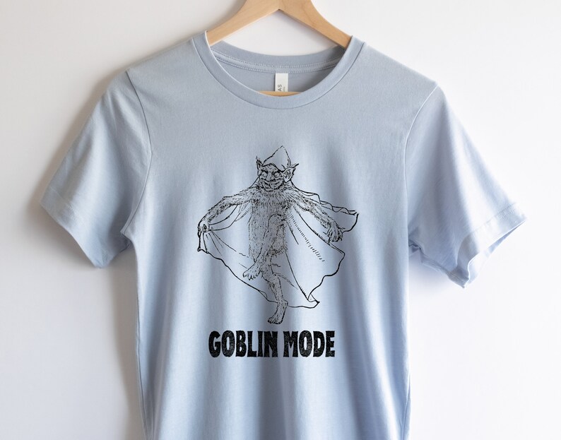 May include: Light blue t-shirt featuring a black and white illustration of a goblin wearing a pointed hat and a cape. The text "GOBLIN MODE" is printed below the illustration.