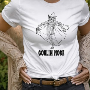 May include: White t-shirt featuring a black and white illustration of a goblin wearing a hat and holding a cape. The text "GOBLIN MODE" is printed below the illustration.
