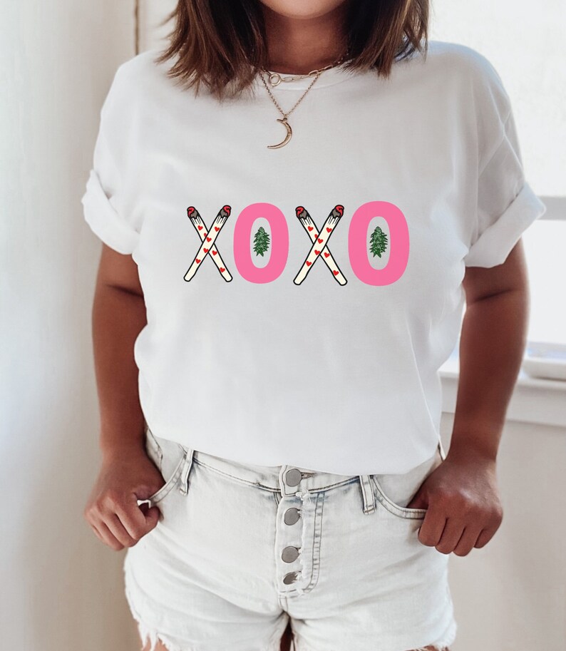 May include: White t-shirt with a pink "XOXO" graphic featuring small red hearts and green Christmas trees.