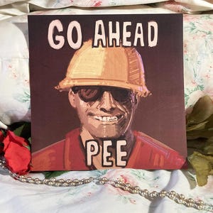May include: A square print featuring a painted illustration of a person wearing a yellow hard hat and dark sunglasses. The text GO AHEAD is printed in light pink above the figure, and the word PEE is printed in light pink below the figure.