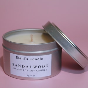 Può includere: Una candela in una lattina argentata con un'etichetta bianca che recita "Eleni's Candle Sandalwood Handmade Soy Candle 113 g / 4 oz".