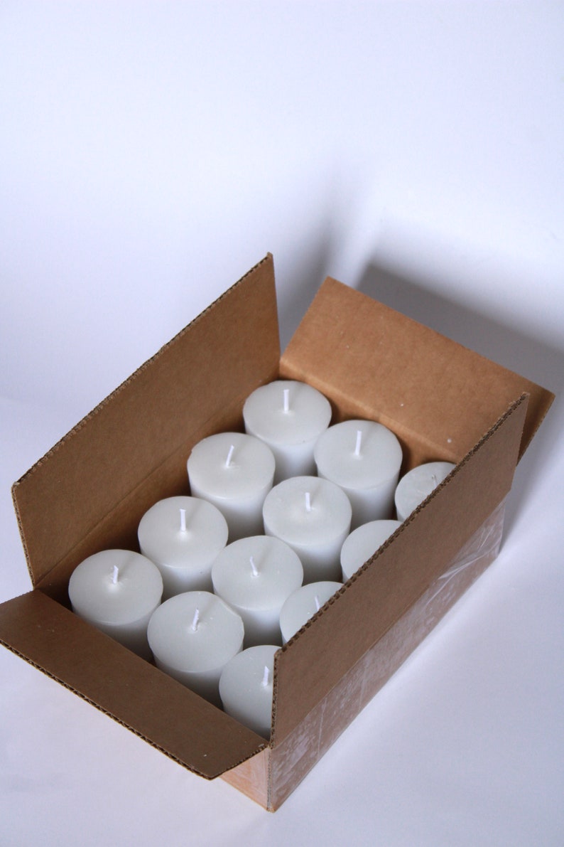 May include: A cardboard box filled with white unscented votive candles. The box is open and the candles are visible inside.