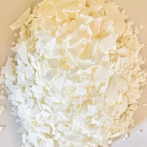 May include: A close-up of a pile of white wax flakes. The flakes are irregular in shape and size, and they are piled high on a white surface.