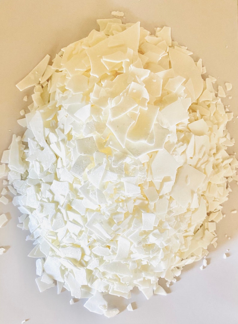 May include: A close-up of a pile of white wax flakes. The flakes are irregular in shape and size, and they are piled high on a white surface.