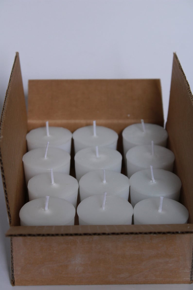 May include: A cardboard box filled with white unscented votive candles. The candles are arranged in rows and are ready to be used.