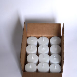 May include: A cardboard box filled with 12 white unscented votive candles.