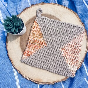 May include: A grey crocheted pot holder with a loop handle. The pot holder has a geometric design with orange and white accents.