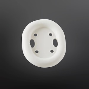 May include: A white, oval-shaped soap dish with a raised rim and four drainage holes. The dish is made of a solid, opaque material and is set against a dark gray background. The design is simple and functional.