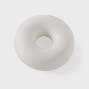 May include: A smooth, white, donut-shaped decorative object. The object has a rounded form with a central circular opening. The surface appears to be matte and uniform in color, with subtle shading.