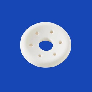 May include: A white, donut-shaped object with a central hole and six smaller holes evenly spaced around the perimeter. The object is set against a solid blue background, creating a clean and minimalist aesthetic.