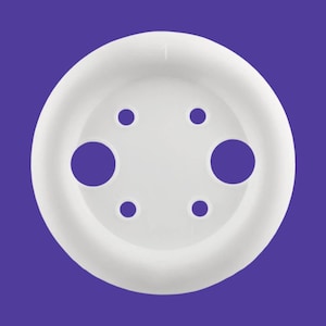 May include: A white, circular object with a series of holes. The object has a raised outer rim and a flat, perforated center. The background is a solid purple color. The object appears to be made of plastic.