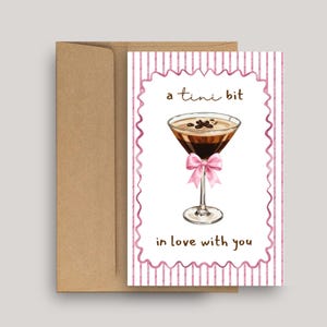May include: Greeting card with a watercolor illustration of a martini glass with coffee beans and a pink bow. The card has the text "a tini bit in love with you" and is inside a brown envelope.