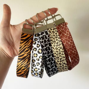 Può includere: Cinque portachiavi con cinturini con stampa animalier. I motivi includono strisce di tigre, macchie di leopardo e stampa giraffa. Ogni portachiavi ha una chiusura e un anello in metallo color argento.