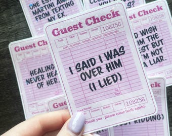 May include: A collection of pink and white guest check stickers with various humorous phrases in black text. One sticker reads "I said I was over him (I lied)." Other stickers have phrases like "One espresso martini away from texting my ex."