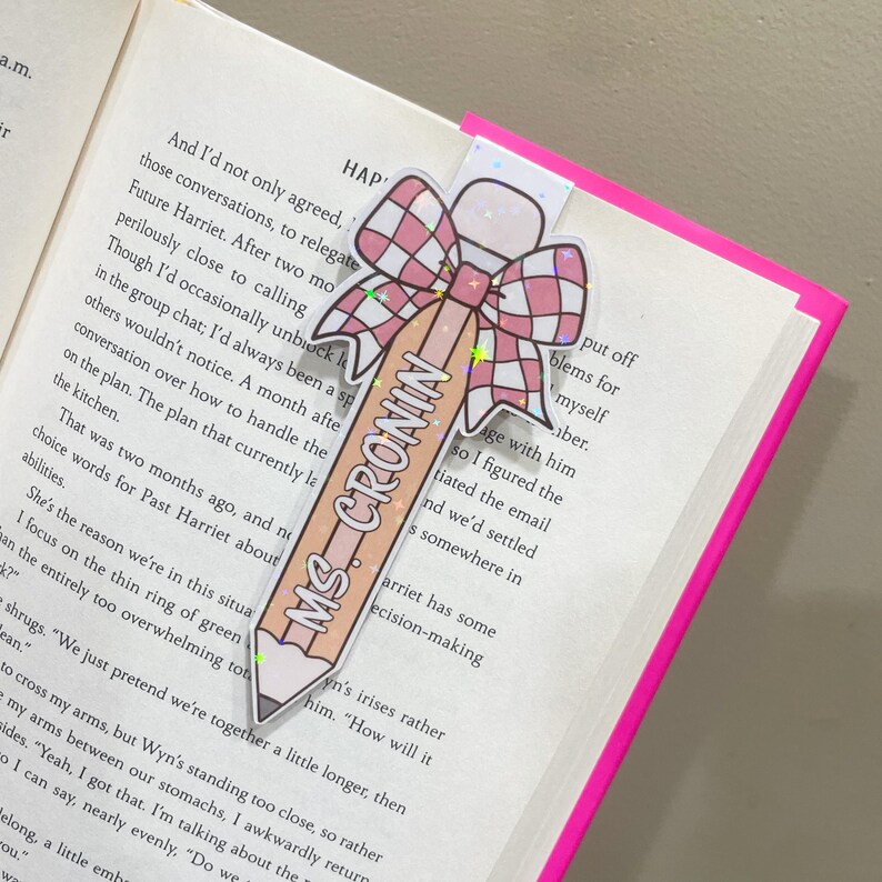 K&ouml;nnte beinhalten: Ein rosa Bleistift mit dem Text "Ms. Cronin" darauf, verziert mit einer rosa und wei&szlig;en karierten Schleife mit einem goldenen Stern. Der Bleistift ist ein Lesezeichen.