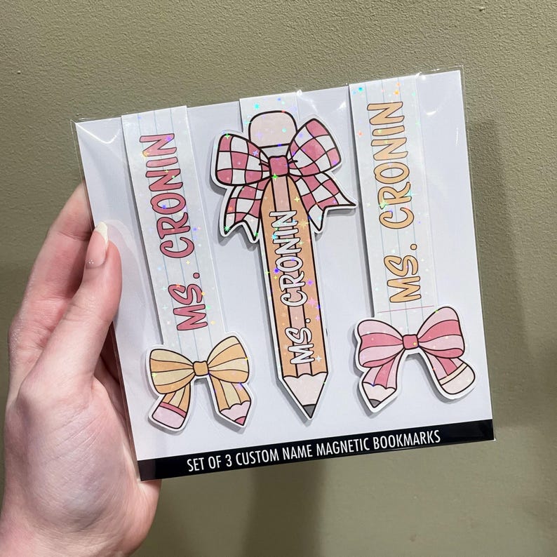 K&ouml;nnte beinhalten: Set mit drei benutzerdefinierten magnetischen Lesezeichen mit einem rosa und wei&szlig;en Bleistift, einer rosa und wei&szlig;en Schleife und einer rosa und wei&szlig;en Schleife mit einem Bleistift. Die Lesezeichen sind mit Glitzer verziert und der Text "MS. CRONIN" ist auf jedem Lesezeichen gedruckt.