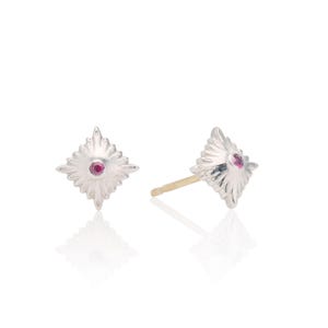 Puede incluir: Un par de pendientes de plata con una piedra preciosa rosa en el centro de cada pendiente. Los pendientes tienen forma de estrella con una superficie texturizada.