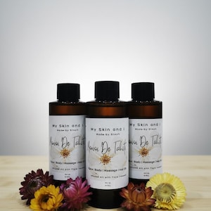 May include: Three brown glass bottles with black caps, labeled "My Skin and I, Monoi De Tahiti." The bottles are surrounded by colorful dried flowers. The product is infused oil with Tiare flowers.