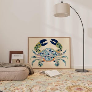 May include: A framed print of a blue, green, and orange crab with white and pink spots on a beige background. The print is hanging on a white wall above a rug with a floral pattern.
