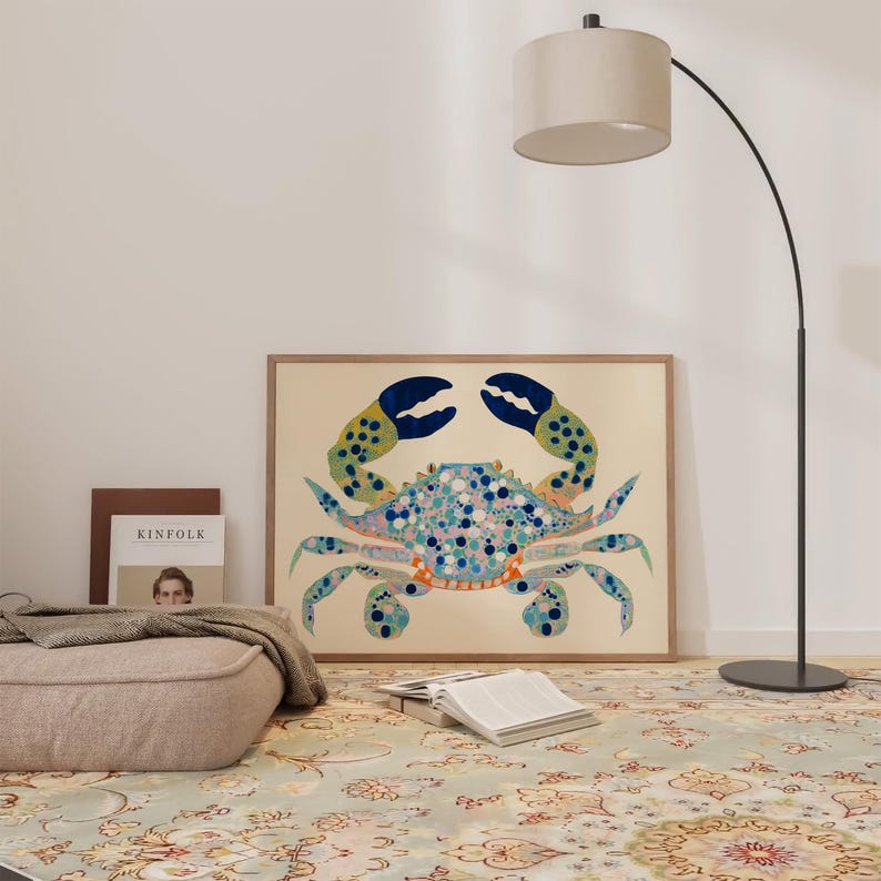 May include: A framed print of a blue, green, and orange crab with white and pink spots on a beige background. The print is hanging on a white wall above a rug with a floral pattern.