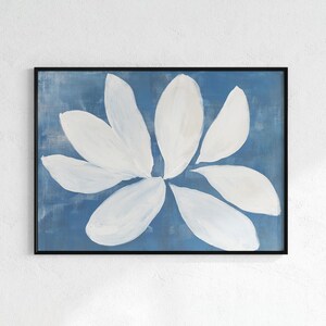 K&ouml;nnte beinhalten: Abstrakter Blumendruck mit einer gro&szlig;en wei&szlig;en Blume vor blauem Hintergrund. Die Bl&uuml;tenbl&auml;tter sind mit breiten Pinselstrichen gemalt und das Kunstwerk ist in einem schwarzen Rahmen gerahmt. Das Gem&auml;lde hat eine moderne &Auml;sthetik.