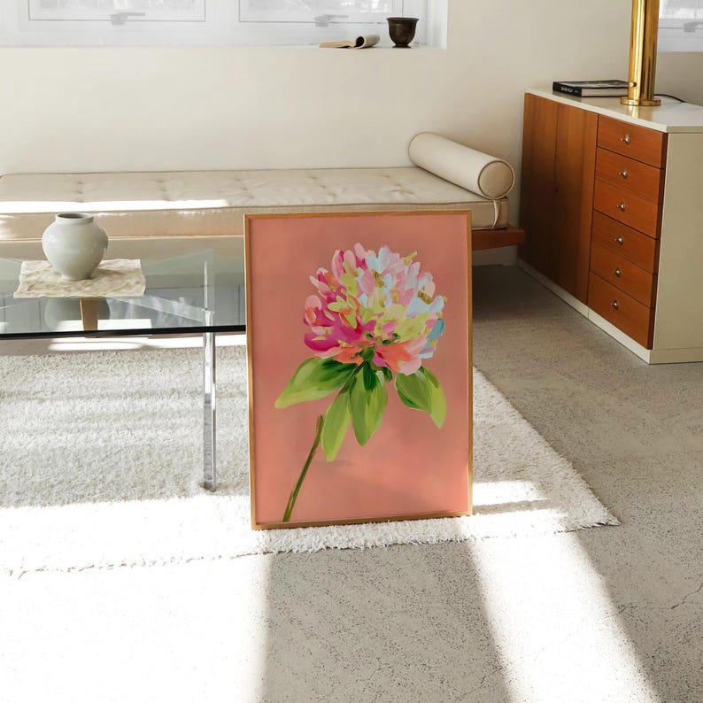 May include: A framed painting of a large, pink flower with green leaves on a peach background.