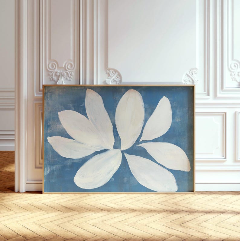 K&ouml;nnte beinhalten: Abstrakter Blumendruck. Eine gro&szlig;e wei&szlig;e Blume vor blauem Hintergrund, gold gerahmt. Das Gem&auml;lde hat eine strukturierte Oberfl&auml;che. Das Kunstwerk wird auf einem Holzboden pr&auml;sentiert. Die &Auml;sthetik ist modern und minimalistisch, passend f&uuml;r die Inneneinrichtung.