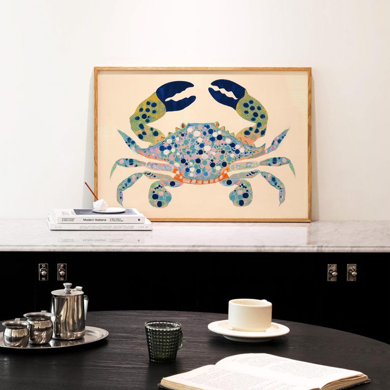 May include: A framed print of a blue and green crab with orange accents and white spots on a cream background.