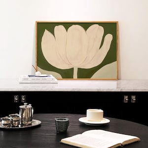 Peut inclure: Une peinture encadr&eacute;e d'un tulip blanc sur fond vert. La peinture est pos&eacute;e sur une surface en marbre blanc avec une pile de livres et un porte-encens en c&eacute;ramique blanche.