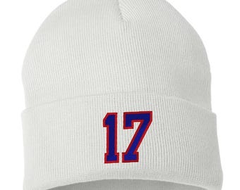 Puede incluir: Gorro de punto blanco con el número 17 azul bordado en la parte delantera. El número está bordeado de rojo.