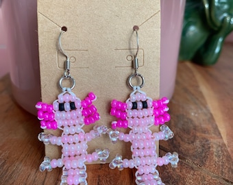 May include: A pair of pink and white beaded axolotl earrings with black eyes. The earrings are hanging from silver hooks.