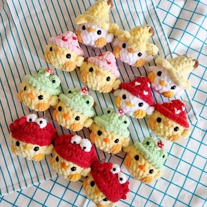 May include: A collection of 13 crocheted chick keychains with various hats. The hats include a mushroom, a witch's hat, a frog, and a red hat with googly eyes. The chicks are all yellow and have black eyes.