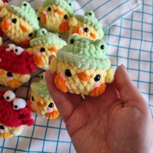 May include: A collection of small crocheted stuffed toys. The toys are shaped like chicks and frogs. The chicks are yellow with orange beaks and black eyes. The frogs are green with black eyes. The toys are all about 3 inches tall.