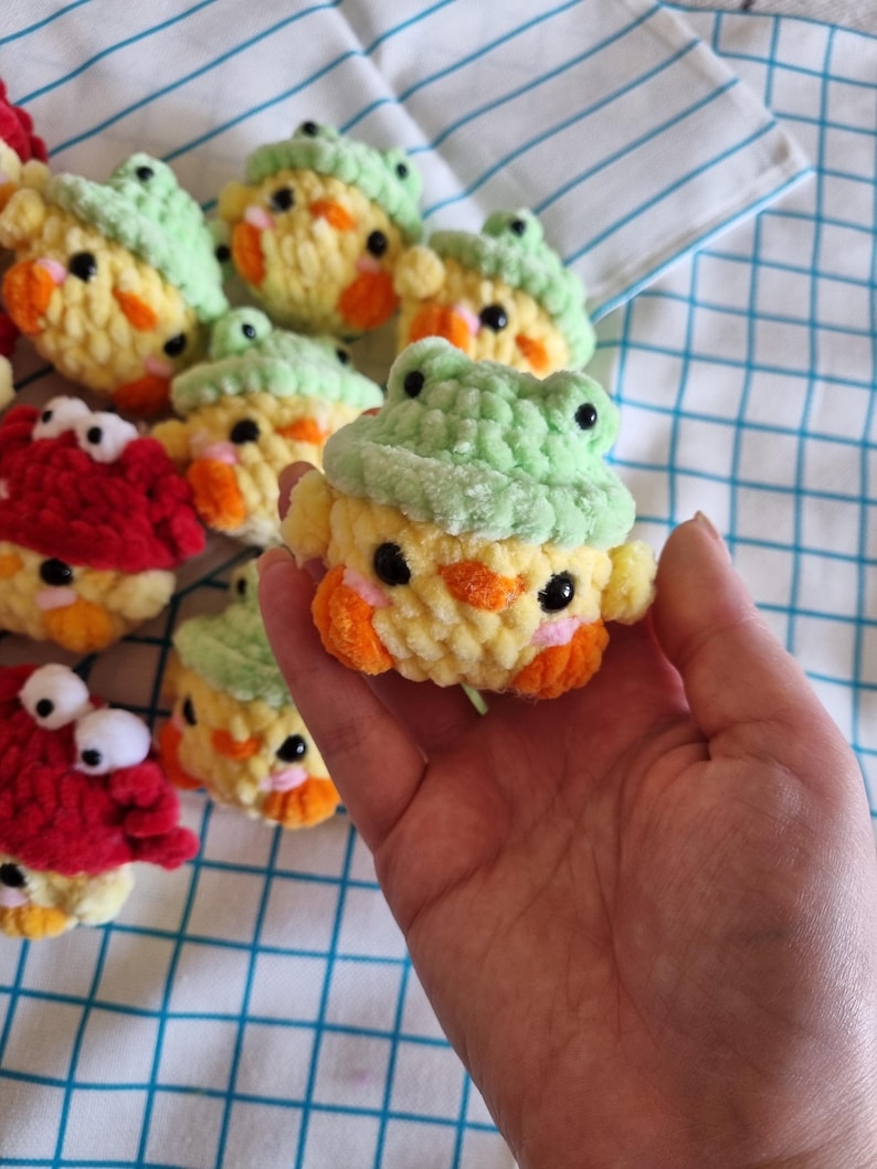 May include: A collection of small crocheted stuffed toys. The toys are shaped like chicks and frogs. The chicks are yellow with orange beaks and black eyes. The frogs are green with black eyes. The toys are all about 3 inches tall.