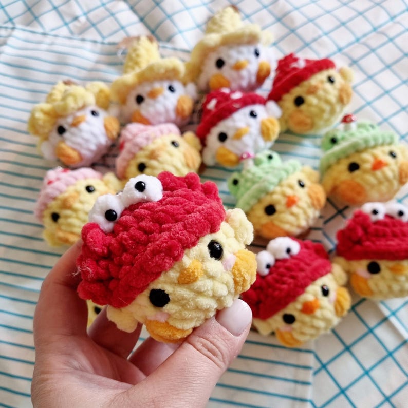 May include: A collection of handmade crocheted chick toys with various colors and designs. Some chicks are wearing hats, while others have large eyes. The chicks are made with soft yarn and have a fluffy texture.