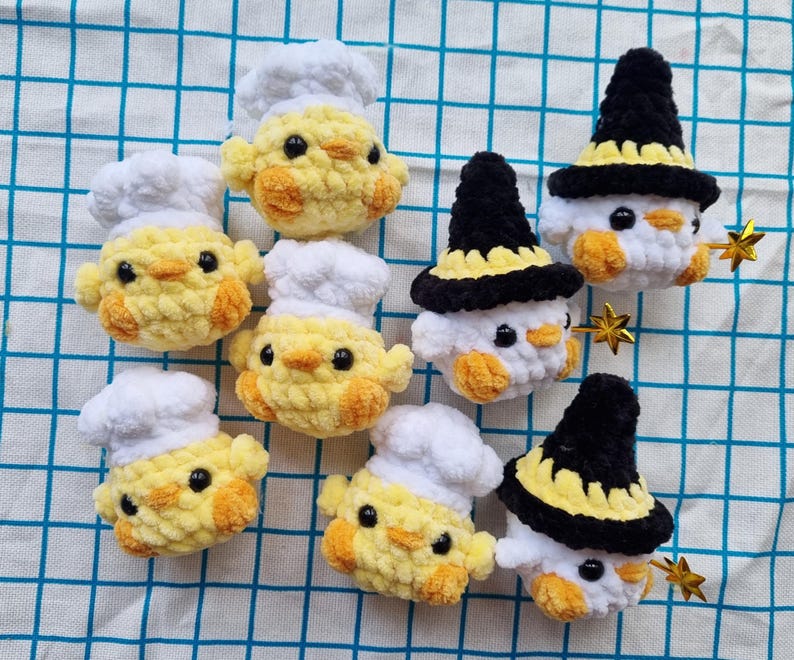 May include: A collection of seven small, crocheted plush figures. Four yellow chicks wear white chef hats, while three white figures wear black and yellow pointed hats. Each figure has black bead eyes and small orange beaks and feet.