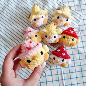 May include: A collection of six crocheted chick keychains. Each keychain features a yellow chick with a different colored hat. The hats include yellow, pink, red, and white. The keychains are perfect for adding a touch of whimsy to your keys or bag.