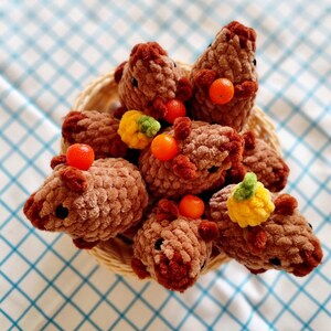 May include: A basket filled with brown plush toys shaped like animals. Each toy has a small orange fruit and a yellow flower attached to it.
