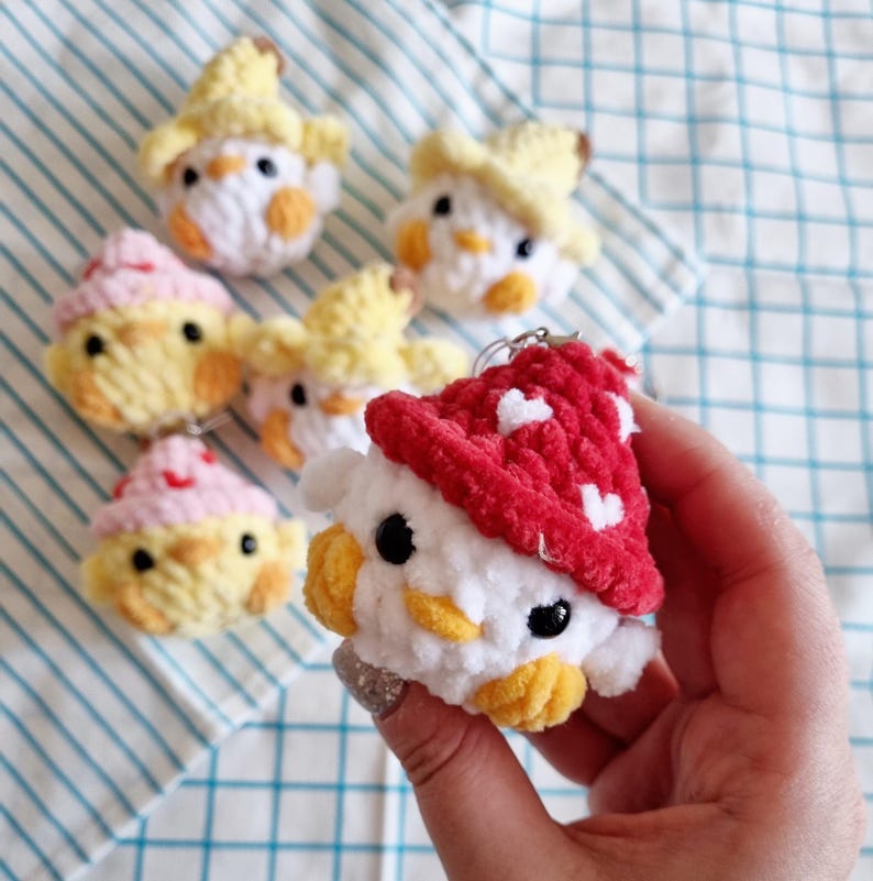 May include: A collection of crocheted plush toys in the shape of chicks. The chicks are wearing different colored hats, including red, yellow, and white. The toys are made with soft yarn and have embroidered eyes and beaks.