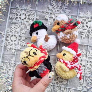 May include: Four handmade crochet Christmas ornaments. Includes a snowman with a black hat, a brown duck with a red and green scarf, a yellow duck with a Santa hat and scarf, and a yellow duck with glasses and a red scarf.