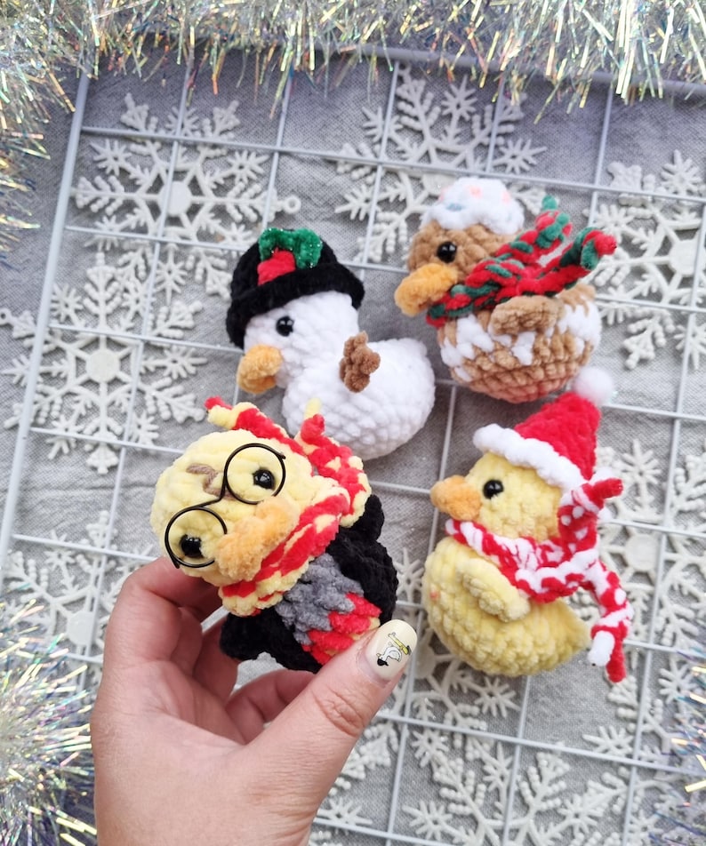 May include: Four handmade crochet Christmas ornaments. Includes a snowman with a black hat, a brown duck with a red and green scarf, a yellow duck with a Santa hat and scarf, and a yellow duck with glasses and a red scarf.