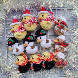 May include: A collection of handmade crochet duck ornaments in various festive designs. Some ducks are yellow with red Santa hats and scarves, while others are white snowmen with black hats. Other ducks wear glasses and scarves.